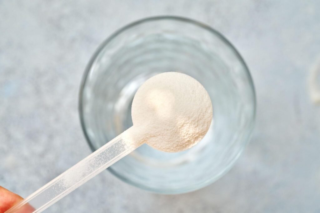 Collagen peptide powder scoop over a glass
