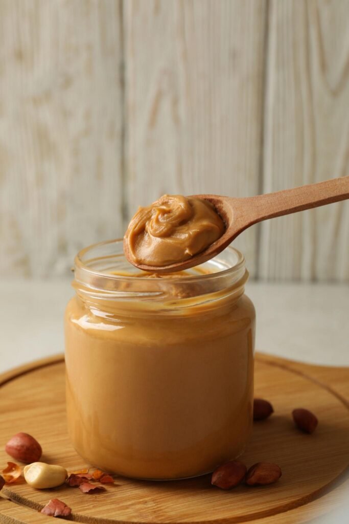 Jar of creamy peanut butter with a wooden spoon and peanuts